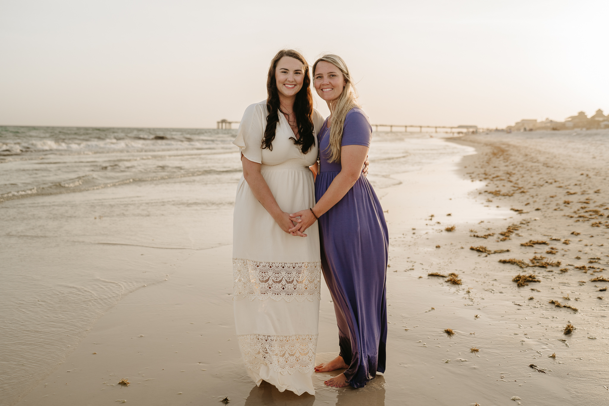 Brides holding hands on beach.